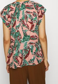 Blusa a maniche corte con tessuto rosa decorato da motivi a foglia verde e bordeaux, orlo peplum e vestibilità morbida.