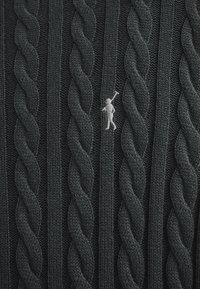 Dunkelgrauer Strickpullover mit einem Zopfmuster und einer kleinen weißen gestickten Figur auf der Vorderseite.