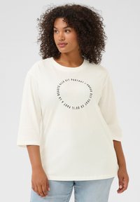 Camiseta de algodón blanca con escote redondo y mangas tres cuartos. Presenta un estampado de texto circular negro en la parte frontal.