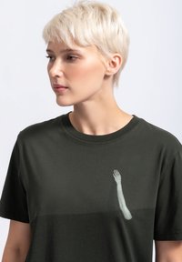 Donkergroen katoenen t-shirt met korte mouwen, voorzien van een lichtgrijs gedrukt armontwerp aan de linkerkant. Soepele textuur, ronde hals.