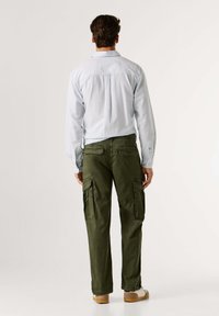 Lichtblauw gestreept overhemd, achterkant zicht; gecombineerd met olijfgroene cargobroek met twee zijzakken en elastische boorden. Glad stoftextuur.