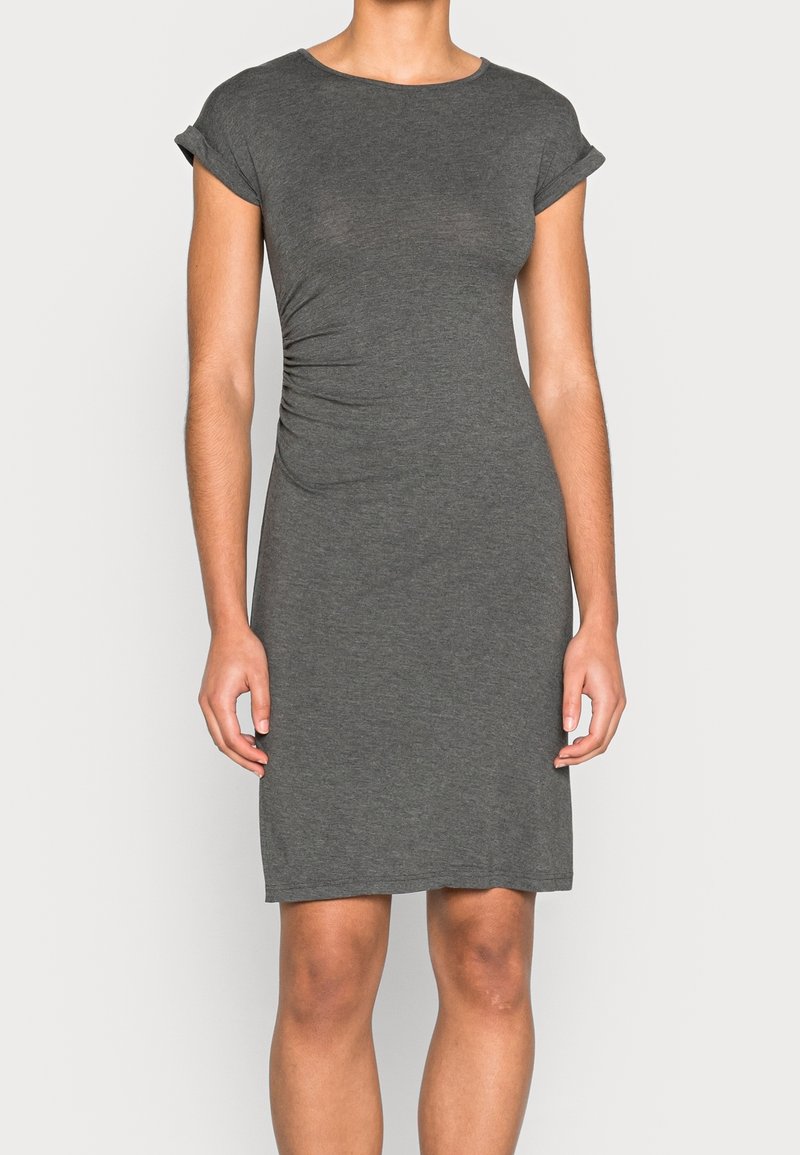 Femme portant une robe grise ajustée à manches courtes et longueur genou avec un léger froncé sur le côté.