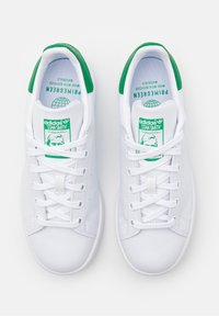 Sneakers bianche Adidas Stan Smith con inserti verdi sul tallone e etichette sulla lingua, viste dall'alto, con lacci e strisce laterali traforate.