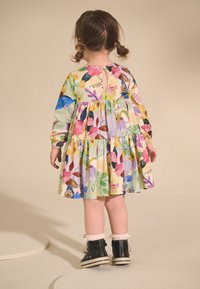 Bloemenjurk in pasteltinten, met lange mouwen, een rok in lagen en een sleutelgat aan de achterkant. Gecombineerd met zwarte enkellaarzen en roze sokken.