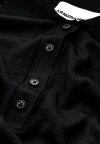 Schwarzes Poloshirt aus strukturiertem Strickstoff, mit einer Knopfleiste mit drei schwarzen Knöpfen und einem Etikett am Kragen.
