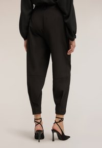 Pantalones negros entallados de tela suave, con cintura alta y puños a la altura del tobillo, combinados con zapatos de tacón alto negros con tiras.