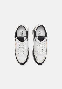 Baskets en cuir blanc et noir avec des clous dorés et des lacets blancs, vues de dessus, montrant le logo Twinset Milano à l'intérieur.