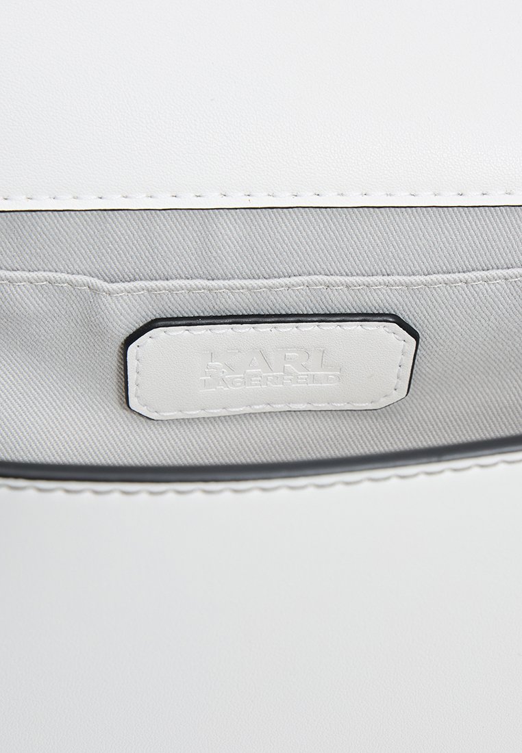 Intérieur d'un sac en cuir blanc avec un revêtement en tissu gris et une étiquette de marque avec une lettrage en relief. Bordure noire le long des coutures.
