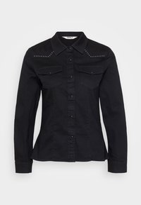 Zwarte denim shirt met lange mouwen, puntige kraag en dubbele borstzakken. Kenmerkt zich door zilveren studs op de schouders en een knoopsluiting aan de voorkant.