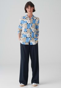 Camicia con bottoni che presenta un audace motivo astratto blu e beige, con maniche lunghe e vestibilità rilassata. Abbinata a pantaloni larghi blu navy.