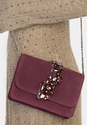 Bordeaux rode suède crossbodytas met een gebogen kristallen versiering, zilveren kettingriem en een gladde flapsluiting. Achtergrond van gestructureerde stof.