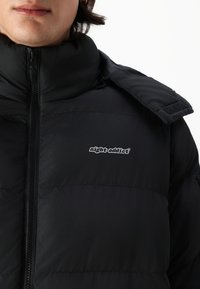 Μαύρο επενδυμένο μπουφάν με ψηλό γιακά, κλείσιμο με φερμουάρ και λογότυπο στην αριστερή πλευρά. Διαθέτει λεία, ματ υφή και λεπτή γυαλάδα.