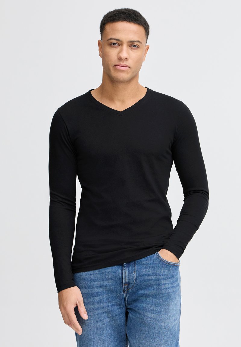 Sort langærmet V-hals skjorte lavet af blødt stof, parret med blå jeans. Designet er tætsiddende og fremhæver torsoen og armene.