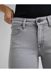 Jeans de mezclilla gris con un diseño ajustado, cintura de altura media, bolsillos frontales y cierre de botón. Tela texturizada con un acabado suave.