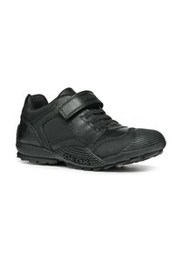 Zapatos de cuero negro con un diseño texturizado, que cuentan con una lengüeta acolchada, una correa de velcro ajustable y una suela de goma con patrón.