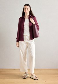 Burgunderfarget satin skjorte, hvit T-skjorte, kremfargede vide bukser, beige sandaler med gull detaljer, og en mørk maroon tote bag.