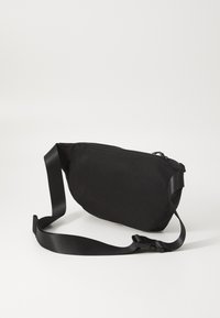 Black fabric sling bag with a curved shape, flat zippered closure, and adjustable strap. Features a smooth texture and minimalist design.
