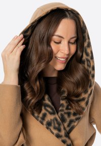 Beżowy płaszcz z kapturem i kołnierzem wykończonym w panterkę. Miękka tkanina, luźny krój, z szerokimi rękawami i klapami z przodu.