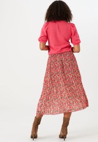 Rosa topp med puffärmar som är kombinerad med en blommig plisserad kjol i röda och rosa nyanser. Bruna ankle boots med utskärningsdetaljer kompletterar outfiten.