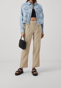 Chaqueta de mezclilla azul clara con patrón floral, top corto negro, pantalones beige de pierna ancha y un pequeño bolso negro texturizado. Sandalias de plataforma marrones.