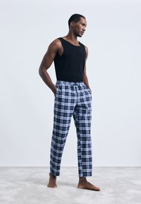 Μαύρη αμάνικη μπλούζα συνδυασμένη με μπλε και λευκό καρό πιτζάμα παντελόνι. Το παντελόνι διαθέτει ελαστική μέση και πλαϊνές τσέπες.