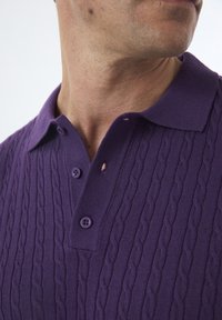 Lilla kabelstrikket polo-shirt med ribbet krave, to knap lukning og et lille hul nær kraven. Tekstureret stoffedetalje.