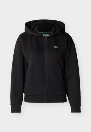 Sweat-shirt à capuche noir avec fermeture éclair, manches longues et petit logo crocodile vert sur la poitrine gauche.