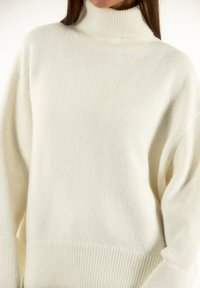 Maglione a collo alto color crema realizzato in morbido materiale a maglia. Presenta un colletto alto, una vestibilità oversize e dettagli a coste nell'orlo e nei polsini.