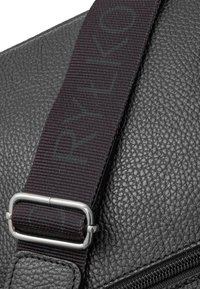 Borsa in pelle nera con una tracolla intrecciata scura caratterizzata da testo stampato. L'hardware metallico collega la tracolla alla borsa, migliorando la robustezza.