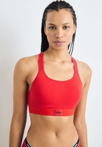 Reggiseno sportivo rosso realizzato in tessuto elastico, con una ampia fascia elastica con logo, design a corsetto e cuciture minimal per il massimo comfort.