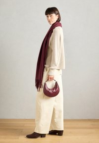 Pull en maille beige, écharpe bordeaux avec franges, pantalons ivoire à jambes larges, sac à main bordeaux en imitation crocodile, bottines à talons marron.