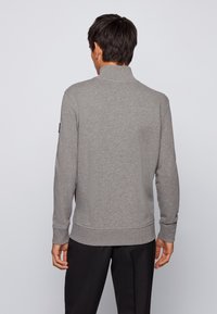 Grå sweatshirt med hög krage, långa ärmar och ribbade cuffs. Mjukt, texturerat tyg; inga synliga logotyper eller mönster. Bärs med mörka byxor.