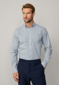 Camicia azzurra con pattern a griglia, maniche lunghe, colletto e bottoni bianchi, abbinata a pantaloni blu navy.