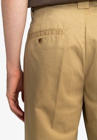 Beige cotton trousers with a back pocket, featuring a button closure. Smooth texture and tailored fit are visible on the side.