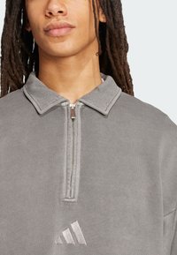 Grå zip-up sweatshirt med krave, ribbet tekstur og broderet logo på brystet. Stoffet ser blødt og afslappet ud.