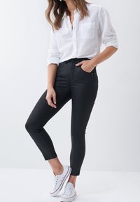 Black skinny jeans made of stretchy denim, paired with a white button-up shirt and white sneakers. Features a high waistband and fitted silhouette.