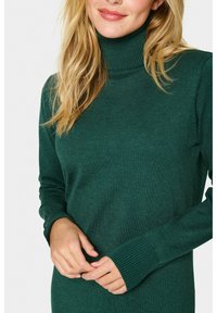 Suéter verde de cuello alto hecho de un suave tejido de punto texturizado. Presenta mangas largas con puños acanalados y una silueta ajustada.