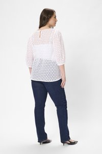 Vit spetsblus med 3/4-långa ärmar och öppen ryggdetalj, i kombination med mörkblå slim-fit jeans och svarta klackskor.
