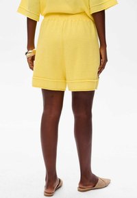 Żółte dziane szorty z elastycznym pasem, wykończonym brzegiem i fakturowanym materiałem, połączone z cielistymi butami wsuwanymi.
