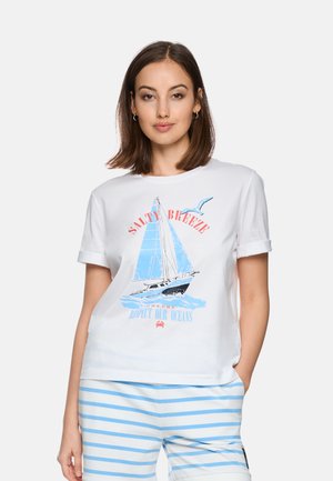 Frau trägt ein weißes T-Shirt mit einem blauen Segelboot- und Möwengrafik sowie dem Schriftzug "Salty Breeze", kombiniert mit weiß-blau gestreiften Shorts.