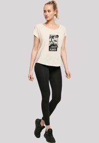 Cream cotton t-shirt with a graphic print, paired with black leggings. Model wears black sneakers. Casual fit with rolled short sleeves.