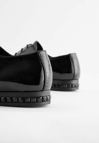 Ballerines noires avec une finition laquée brillante, des accents texturés en embossage crocodile et une semelle extérieure noire cloutée.
