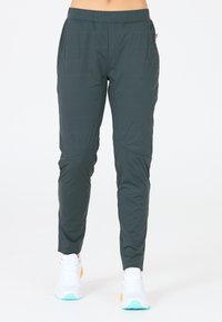 Donkergroene sportbroek met een taps toelopende pasvorm, gemaakt van lichtgewicht stof. Heeft een zachte textuur en schuine naden, gecombineerd met witte sneakers.
