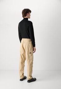 Svart langermet topp kombinert med beige cargo bukser, med elastisk liv, sidelommer og en avslappet passform; svarte sko fullfører antrekket.