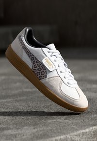 Baskets blanches avec des accents en daim et en cuir. Présentent un panneau latéral en imprimé léopard, un col rembourré et une semelle en caoutchouc texturée. Détail en logo doré.