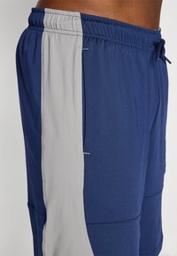 Tengerészkék és szürke sportpantalók gumis derékkal, kontrasztos szürke oldalsó panelekkel és díszőrölt varrási részletekkel.