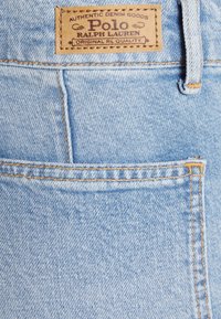 Light blue denim fabric with a leather label featuring "Polo Ralph Lauren" embossed in brown, visible stitching and a back pocket.