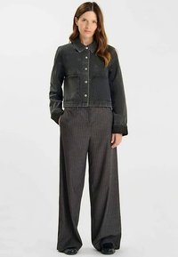 Veste en denim noir avec fermeture à boutons et deux poches frontales, associée à un pantalon large à rayures aux teintes sombres.