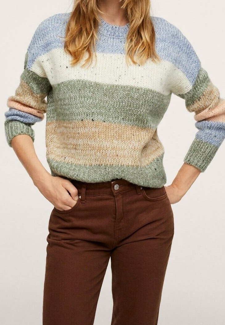 Femme portant un pull en tricot à rayures pastel et un pantalon marron taille haute, les mains posées sur les hanches.