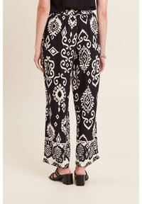 Zwart-witte gestreepte wijde broek met een elastische tailleband, voorzien van een opvallend tribaal ontwerp en een zachte, lichte stof.